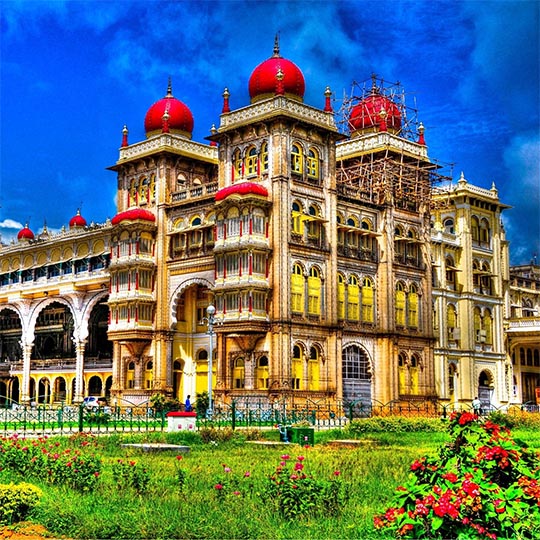 An ornate Indian palace with red domes and arched facades, behind a garden of flowers.