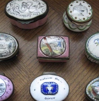 A collection of small painted enamel snuff boxes on a wooden table, one inscribed Esteem the Giver.